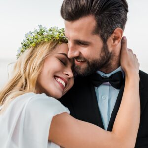 affectionate wedding couple in suit and white dress hugging on beach